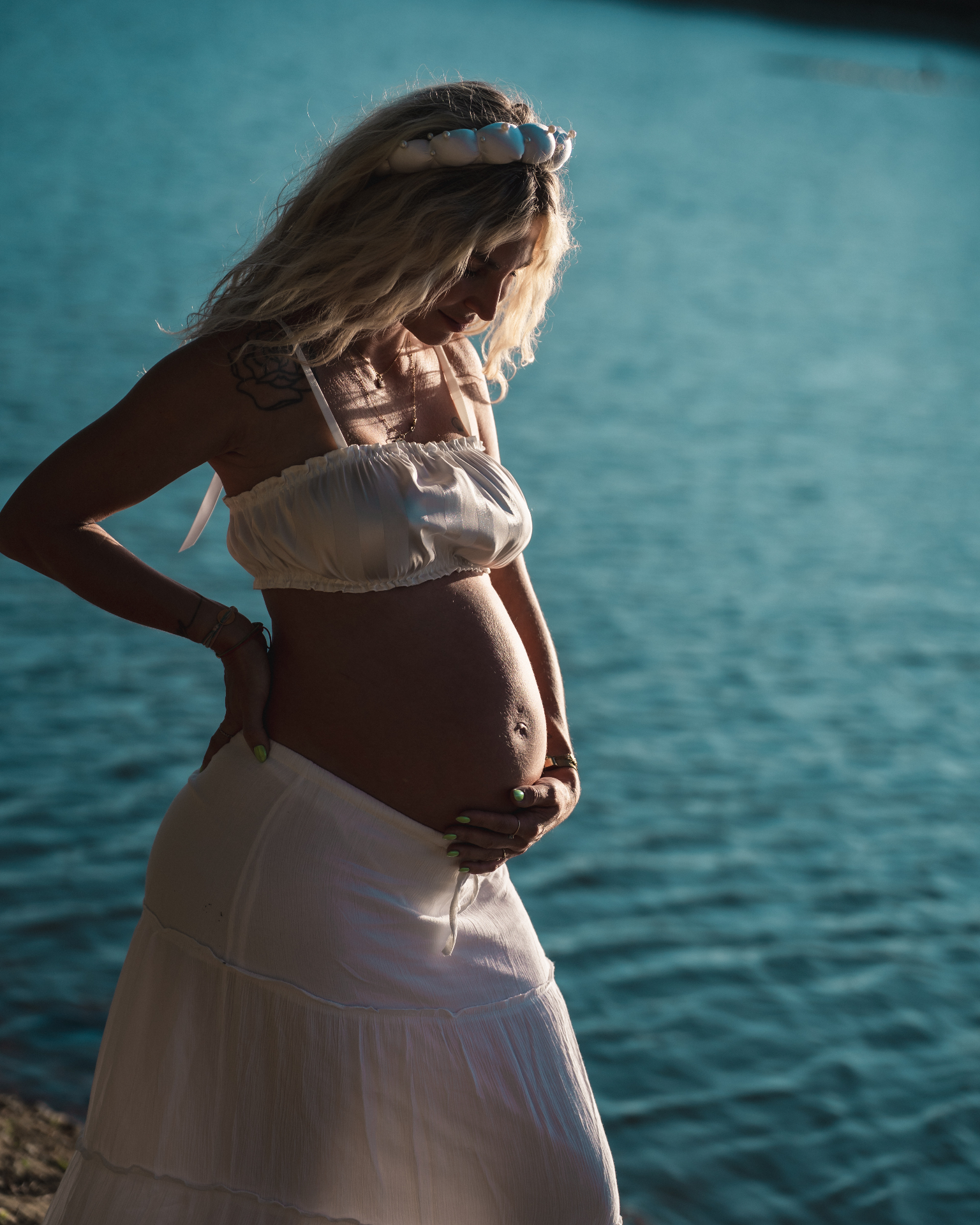 Future maman en robe blanche devant l'eau turquoise