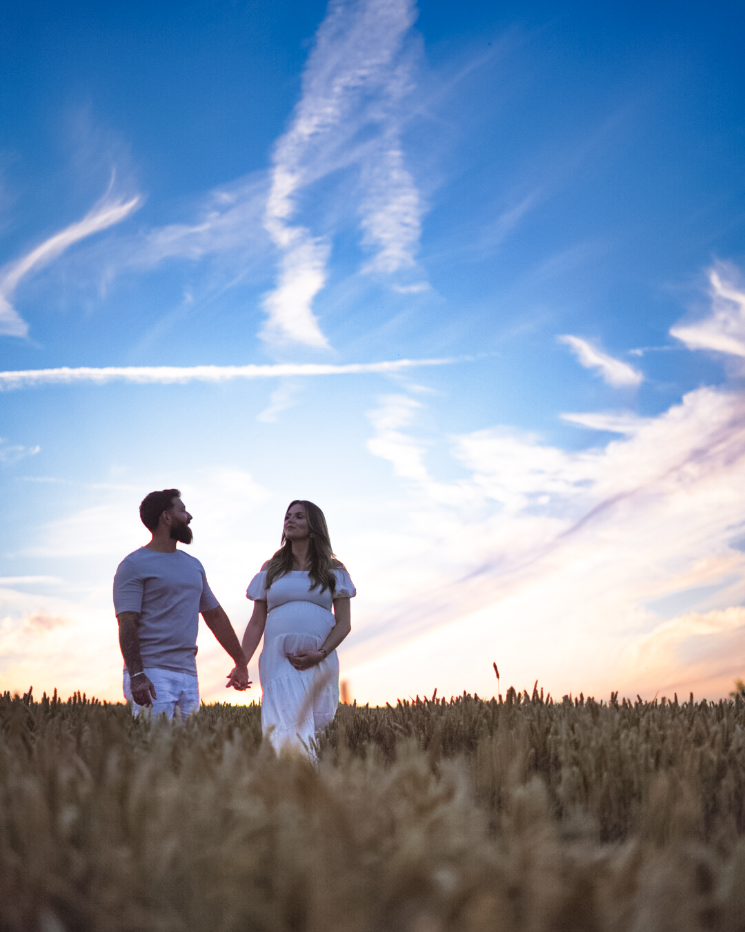 Couple attendant bébé dans un champ de blé au coucher du soleil